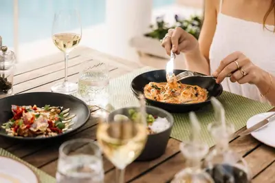 a woman eating food on a table with glasses of wine at Birkenhead House in Hermanus