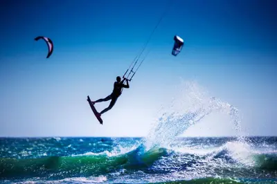 a man is in the air over the ocean at Unwind at Coral 2BR Bloubergstrand Beach Apt Walk to Beach in Bloubergstrand