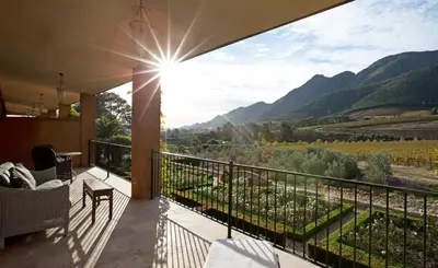 a balcony with a view of a vineyard and mountains at La Residence in Franschhoek