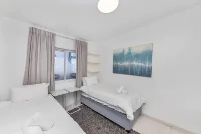 a white room with two beds and a window at Horizon Bay 202 Beachfront APT, Bloubergstrand in Cape Town
