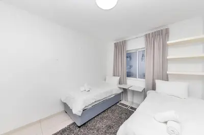 a white bedroom with two beds and a window at Horizon Bay 202 Beachfront APT, Bloubergstrand in Cape Town