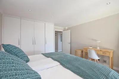 a white bedroom with a bed and a desk at Dolphin Beach Estate 131sm in Cape Town