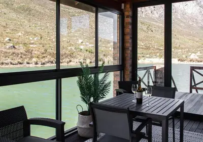 a table and chairs on a porch with a view of the water at Wildeberg Dam House Cottage in Franschhoek