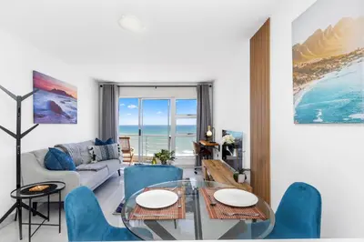 a living room with a glass table and blue chairs at The Bay A602 in Cape Town