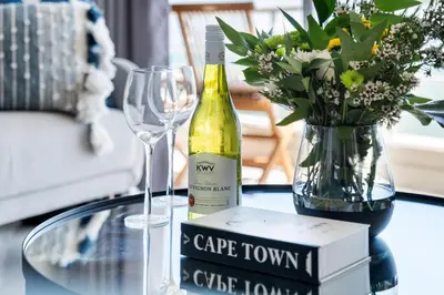 a bottle of wine sitting on a table with a vase of flowers at The Bay A602 in Cape Town