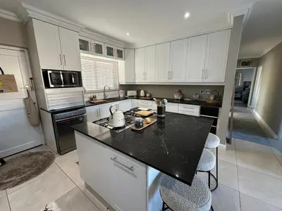 a kitchen with white cabinets and a black counter top at Strand Holiday home in Cape Town
