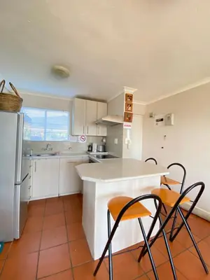 a kitchen with white cabinets and orange chairs in it at The Hermanus holiday self catering beach club in Hermanus