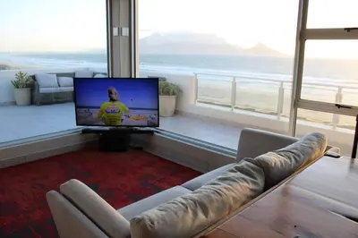 a living room with a couch and a tv in a room at Jacuzzi with 270 views right on beach in Cape Town