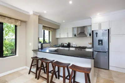 a kitchen with white cabinets and bar stools at Luxury Lodge 4F Pearl Valley Golf Estate in Simondium