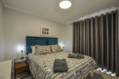 a bedroom with a bed with a blue headboard and curtains at Pet friendly & Close to Beach at 2 Saasveld in Bloubergstrand