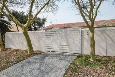 a garage with a white fence and two trees at Pet friendly & Close to Beach at 2 Saasveld in Bloubergstrand