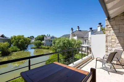 a balcony with a wooden table and chairs and a river at Pearl Valley Golf Estate Lodge 1E in Simondium