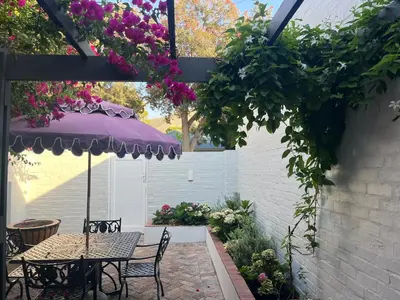 a patio with a table with a purple umbrella and flowers at On Musson in Hermanus