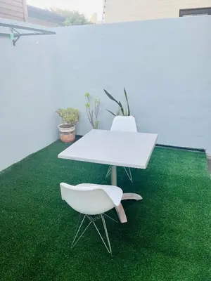 a white table and a chair on a green carpet at Self catering one bedroom cottage in Cape Town