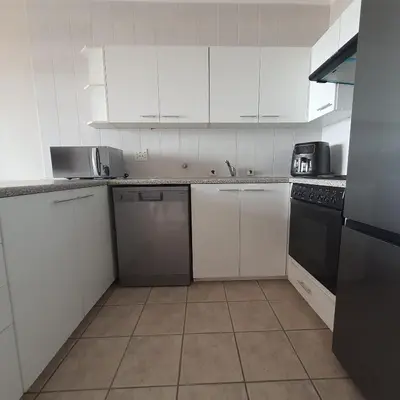 a white kitchen with white cabinets and black appliances at 215 Sea View in Cape Town