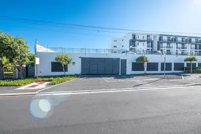 a white building with a garage in front of a street at Top Floor Beachfront w Views, Blouberg, 51 Beach Break in Bloubergstrand