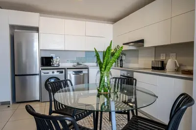 a glass table with chairs and a vase with a plant at Top Floor Beachfront w Views, Blouberg, 51 Beach Break in Bloubergstrand