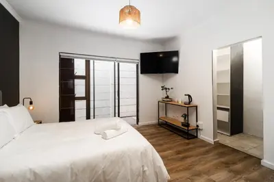a bedroom with a white bed and a television at En-suite Room, Walking distance to Kite Beach in Cape Town