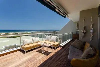 a balcony with a couch and a table and a view of the ocean at Dolphin Hill Apartment, Cape Town, Dolphin Beach in Cape Town