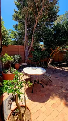 a patio with a table and chairs and trees at The Sculpture Yard in Gordonʼs Bay