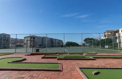 a tennis court with green grass and a fence at Hermanus Beach Club 104 in Hermanus