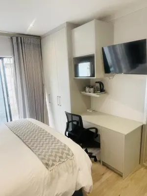 a bedroom with a bed and a desk and a tv at Private Luxury Room by 29 Holborn in Cape Town
