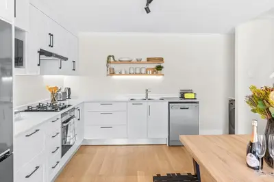 a white kitchen with white cabinets and a wooden table at 2D on Nansen in Cape Town