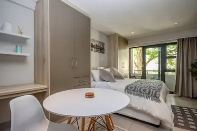 a bedroom with a bed and a white table and chairs at 23 On The Den Studio Apartment in Stellenbosch