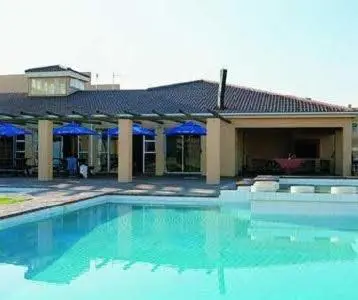 a swimming pool in front of a building with blue umbrellas at Unit 75 Hermanus Beach Club in Hermanus