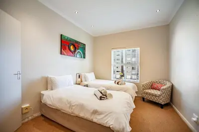 two beds in a room with a chair and a window at Coral Breeze Walk to Everything in Cape Town
