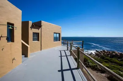 a building with a walkway next to the ocean at Villa Sur La Mer in Pringle Bay