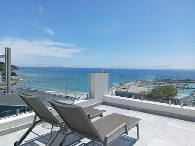 a patio with chairs and a table and the ocean at 34 Gordonia, Beachfront Penthouse in Gordonʼs Bay
