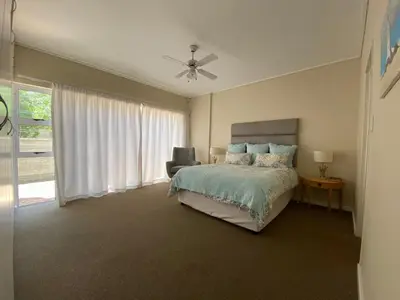 a bedroom with a bed and a chair and a window at Onrus Beach House in Hermanus