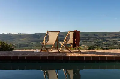 two chairs sitting on a dock next to a swimming pool at Spioenkop Wines Farm House in Elgin