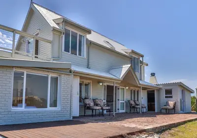 a house with rocking chairs on a patio at Penguin's Nest in Bettyʼs Bay