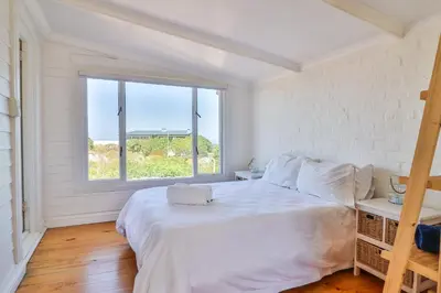 a bedroom with a large white bed and a window at Penguin's Nest in Bettyʼs Bay