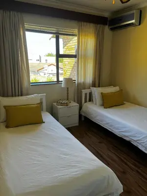 two beds in a room with a window at Gordon's Bay Townhouse in Gordonʼs Bay