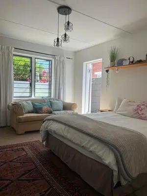 a bedroom with a bed and a couch and windows at Serene Studio in Cape Town