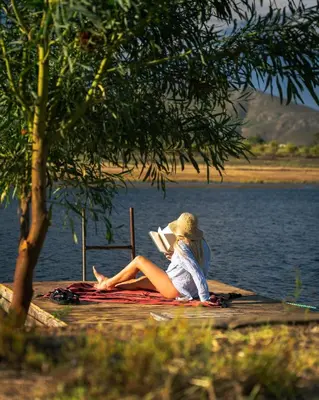a woman sitting on a dock reading a book at Natimby Lodge in Botrivier