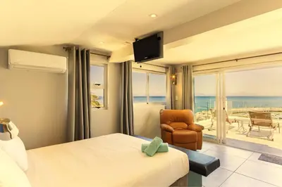 a hotel room with a bed and a chair and a balcony at Bikini Beach Townhouse in Gordonʼs Bay
