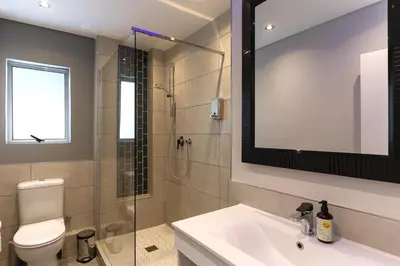 a bathroom with a shower and a toilet and a sink at Bikini Beach Townhouse in Gordonʼs Bay