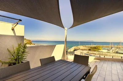 a wooden table and chairs on a balcony with the ocean at Bikini Beach Townhouse in Gordonʼs Bay