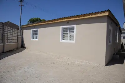 a white building with two windows and a brick driveway at one bedroom apartment A1 in Cape Town
