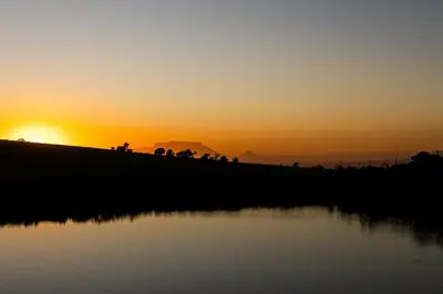 a sunset over a field with a body of water at Amperbo Glamping in Cape Town