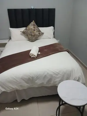 a white bed with a wooden headboard and a table at The Gem Guest House & Spa in Parow
