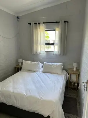 a bedroom with a bed with white sheets and a window at Seewind in Hermanus