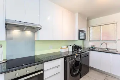 a kitchen with white cabinets and a washer at Sea Spray B303 by CTHA in Cape Town