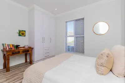 a white bedroom with a bed and a wooden table at Val de Vie in Simondium