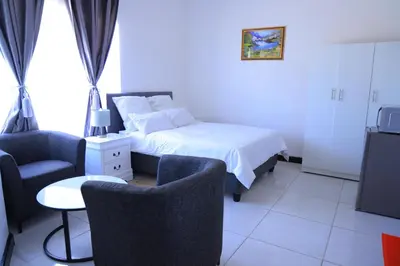 a bedroom with a bed and two chairs and a tv at paradise guest house in Cape Town