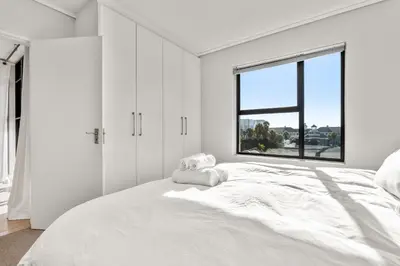 a white bedroom with a large bed with a window at Waters Edge Luxury Apartment Century City in Cape Town